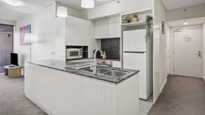 A modern kitchen with white cabinetry, a granite countertop, a built-in microwave, and a stainless steel sink. - Brisbane City Retreat With Private Balcony (Brisbane)