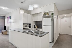 Uma cozinha moderna com armários brancos, bancada de granito, micro-ondas embutido e pia de aço inoxidável.