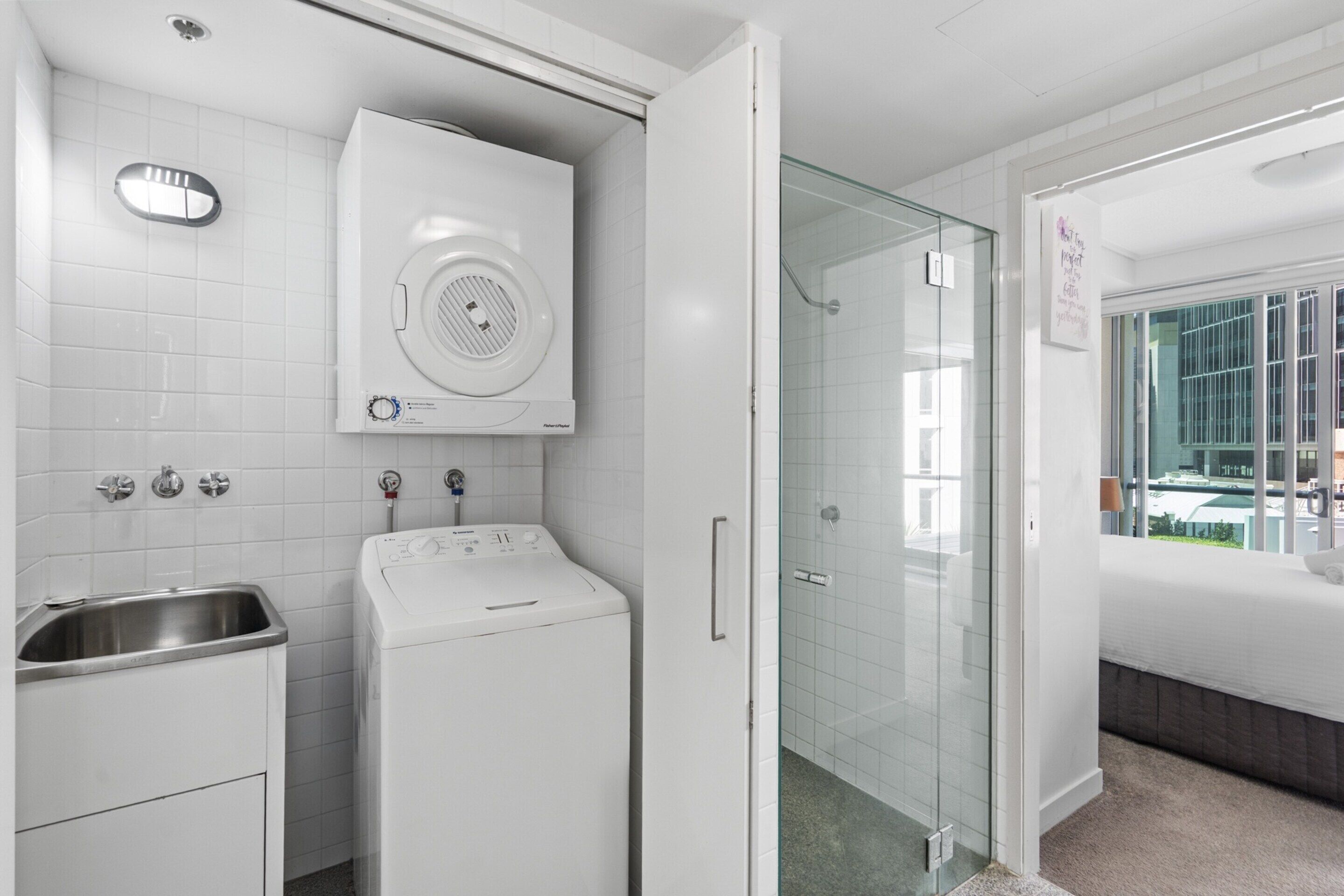A modern bathroom with a washing machine, a sink, and a glass shower enclosure.