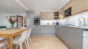 Een moderne keuken met grijze kastjes, een houten eettafel en witte stoelen.