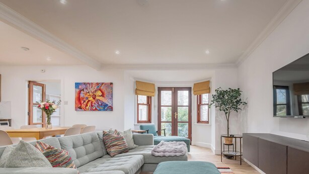 Een ruime woonkamer met een grote bank, een televisie en een eethoek met een tafel en stoelen.