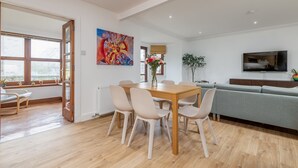 Een moderne eethoek met een houten tafel en stoelen, een bank en een aan de muur bevestigde televisie.