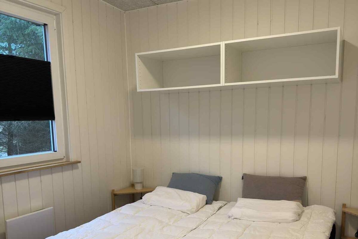 A bedroom with a bed, two nightstands, a window with blinds, and a ceiling with a grid pattern.