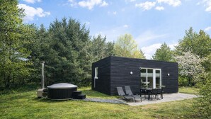 Une cabane moderne de couleur noire, dotée d’un bain à remous, d’un espace salon extérieur et d’une terrasse.