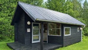 Une petite cabane en bois sombre, avec un toit en métal, une porte d’entrée et un petit porche.