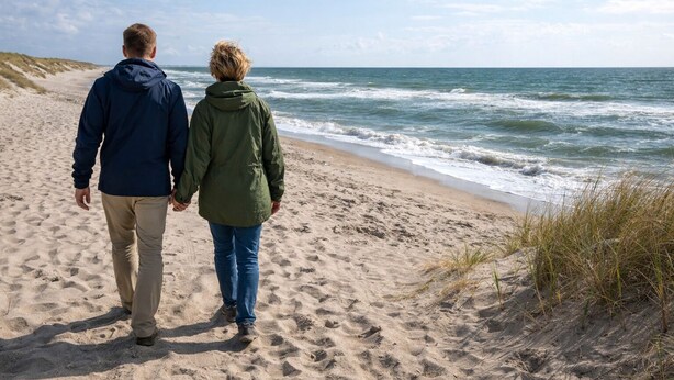 Deux personnes se promènent sur une plage de sable, avec l’océan en arrière-plan.