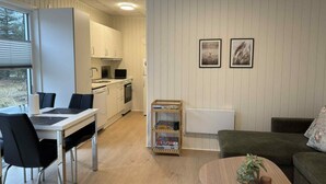 Une cuisine moderne avec des meubles blancs, une table à manger avec des chaises, une petite table basse et une bibliothèque contenant des jeux de puzzle.