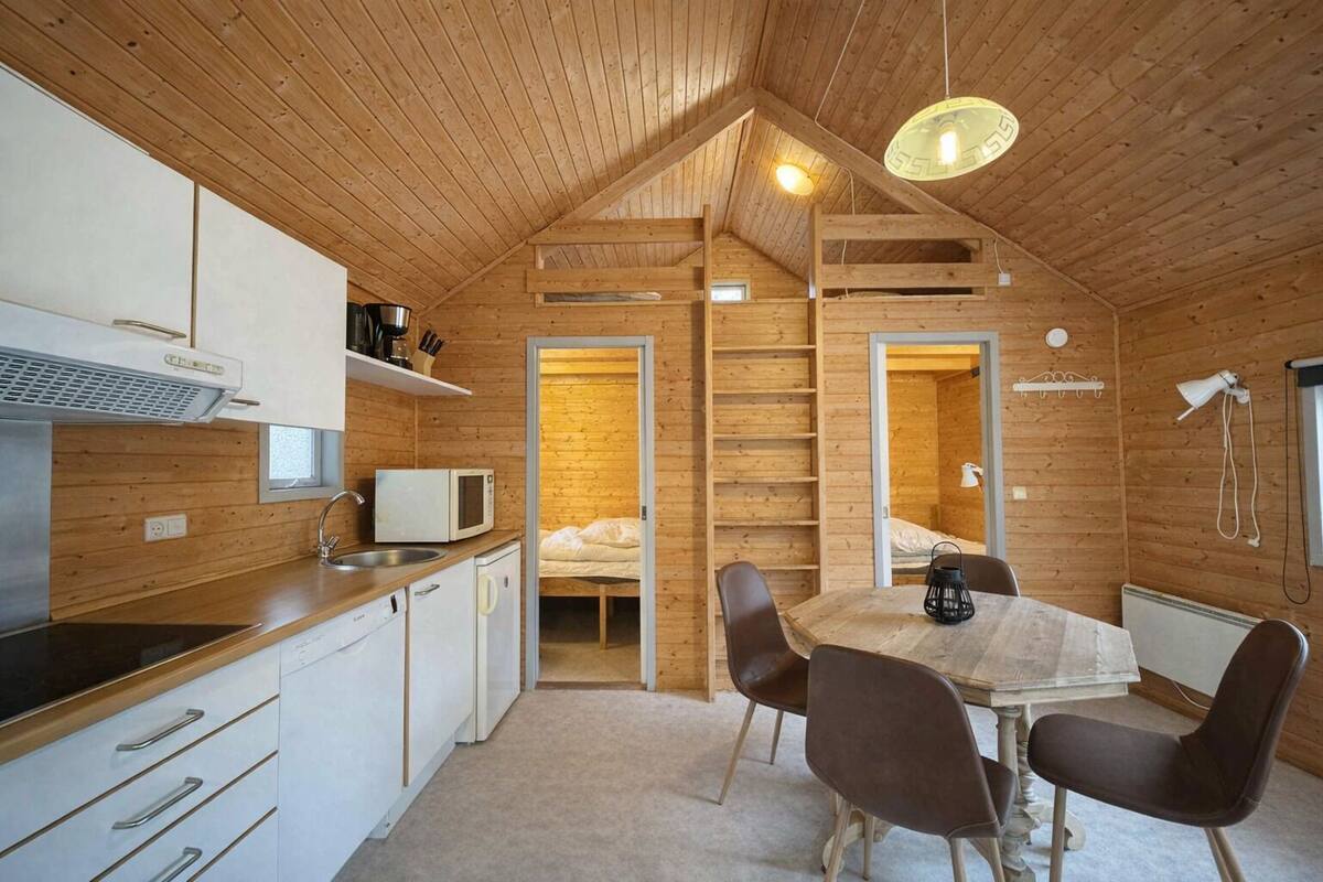 A compact, wooden cabin-style kitchen with a dining area, a built-in microwave, and a ladder leading to a loft bedroom.