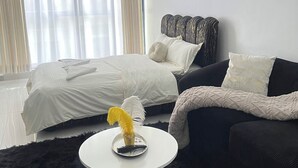 A modern bedroom with a bed, a sofa, a small round table, and a large window with curtains. - Modern studio close to JKIA and SGR Syokimau (Nairobi)