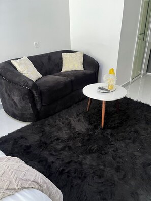 A modern living room with a black sofa, two decorative pillows, a white coffee table, and a fluffy rug. - Modern studio close to JKIA and SGR Syokimau (Nairobi)