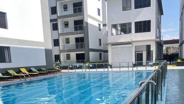 A swimming pool with a metal railing, surrounded by modern buildings with balconies. - Modern studio close to JKIA and SGR Syokimau (Nairobi)