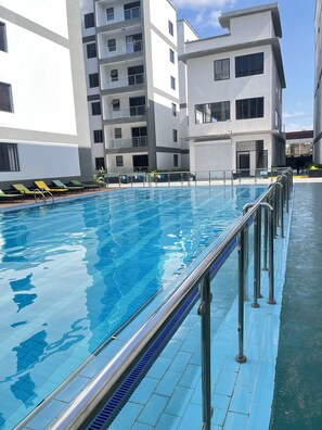 En swimmingpool med ett metallräcke, omgiven av moderna byggnader med balkonger.