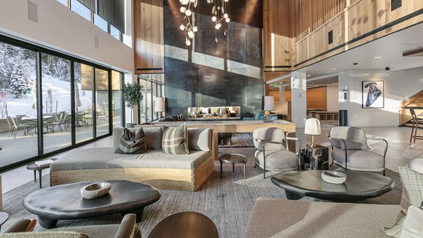 A spacious living area with a large sofa, coffee table, and seating arrangement. A kitchen area is visible in the background with a dining table and chairs. - Ski-in/out Deer Valley Resort Pool 3br 3 Bedroom Condo (Park City)