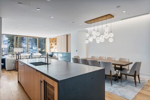 A modern kitchen with a large island, wooden cabinets, and a dining area with a table and chairs. - Ski-in/out Deer Valley Resort Pool 3br 3 Bedroom Condo (Park City)