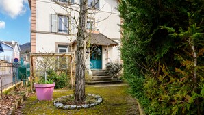 A residential building with a front door, steps, and a garden with a tree and a pink planter. - Apartment Le 47: Spacious Holiday Home with Wi-Fi in Alsace (Thann)
