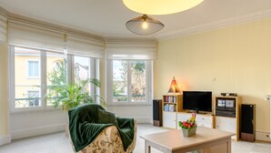 A living room with a bean bag chair, a table with a flower vase, a television, and speakers. - Apartment Le 47: Spacious Holiday Home with Wi-Fi in Alsace (Thann)