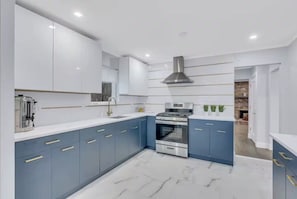 A modern kitchen with white and blue cabinetry, a stainless steel stove, and a large window. - Hot Tub Fire Pit Huge Yard Dual Homes Sleeps 18 (Suffern)
