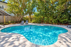 A swimming pool with a curved edge, surrounded by a wooden deck and a wooden fence. - Bay Esplanade By GoldenCoastRentals (Clearwater)