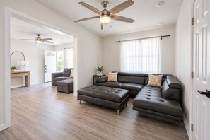 Ein geräumiges Wohnzimmer mit einem Ecksofa, einem Couchtisch und einem Deckenventilator.