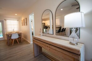 Eine moderne Küche mit weißen Schränken, einem Holztisch mit Stühlen und einem großen Spiegel über der Arbeitsfläche.