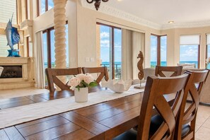A dining area with a view of the ocean, a fireplace, and a decorative seahorse. - Vista del Mar by GoldenCoastRentals | Beachfront Villa • 6BR + Loft • 7 Baths • Game Room (Indian Rocks Beach)