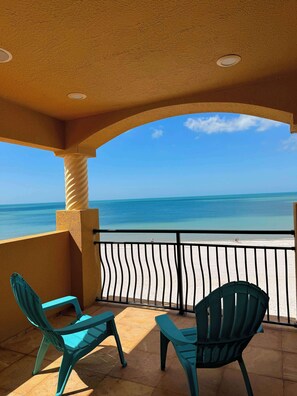 A balcony with two turquoise chairs, a view of the ocean, and a clear sky. - Vista del Mar by GoldenCoastRentals | Beachfront Villa • 6BR + Loft • 7 Baths • Game Room (Indian Rocks Beach)