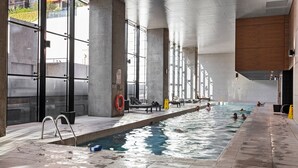 Piscina interior com paredes de vidro transparente, corrimãos de metal e chão revestido de azulejos.