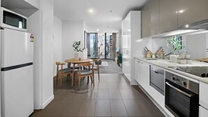 Uma cozinha moderna com armários brancos, uma área de jantar com mesa e cadeiras, e vista para a paisagem urbana através de grandes janelas.