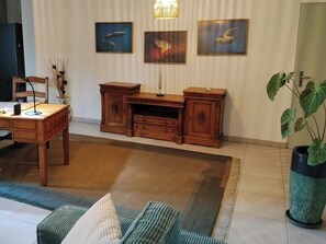 A living room with a wooden desk, a chair, a sofa, and a large potted plant. There are three framed pictures on the wall. - Vacation apartment with terrace and small garden (St. Leu)