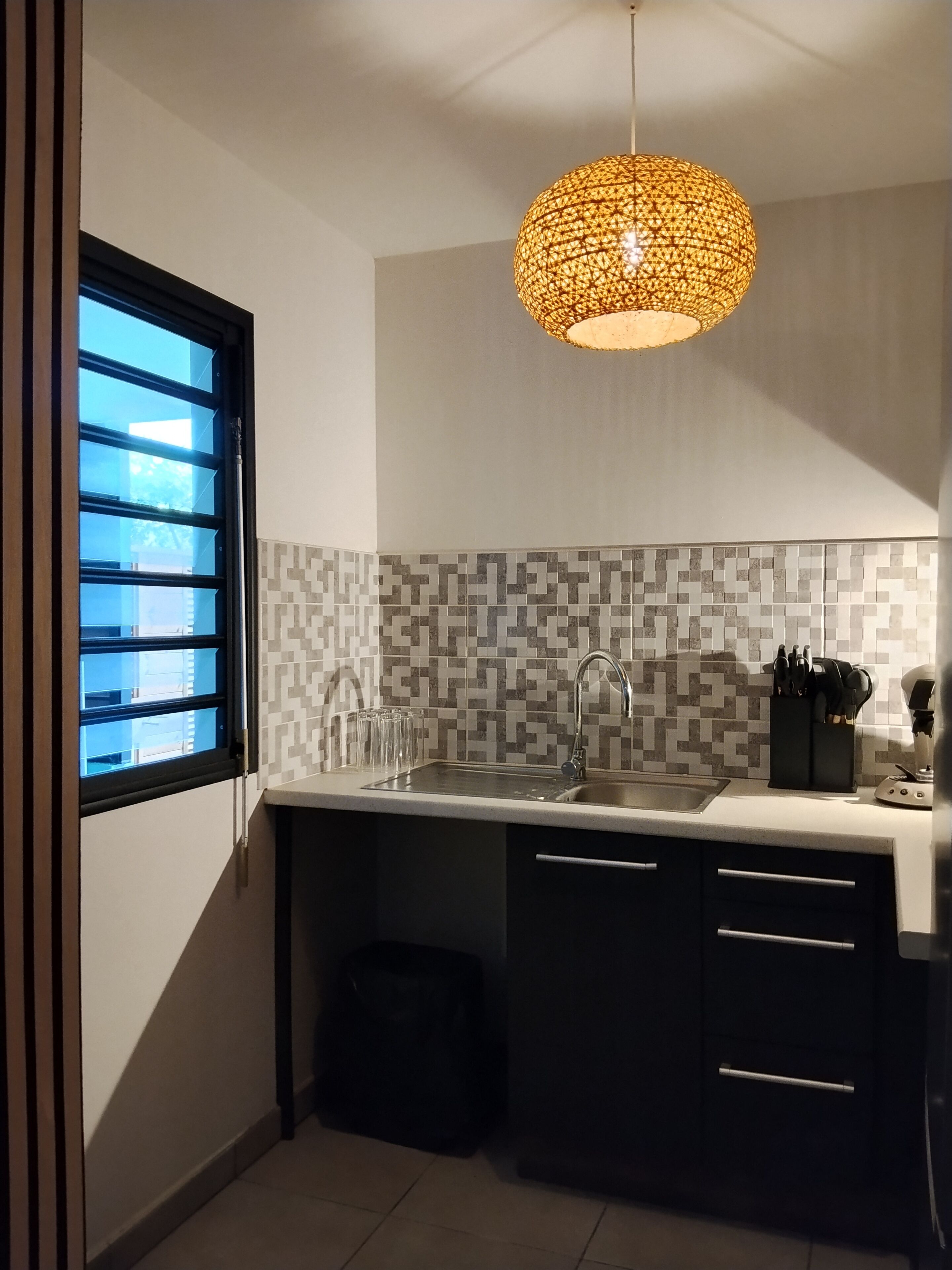 Una cucina dal design moderno, con uno schienale geometrico, un lavello in acciaio inossidabile e una lampada a sospensione.