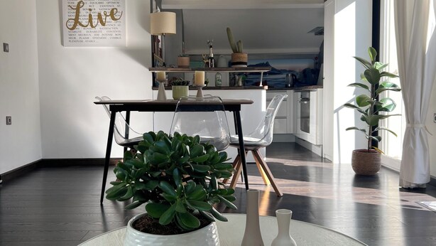 Ein modernes Wohnzimmer mit einem runden weißen Tisch, einer Topfpflanze und minimalistischer Einrichtung.