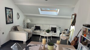 Ein modernes Wohnzimmer mit einem weißen Sofa, einem Esstisch mit Platzdeckchen mit Hirschmuster, einem kleinen runden Tisch mit Kerzen und einem Bücherregal mit Büchern und Dekorationsobjekten.