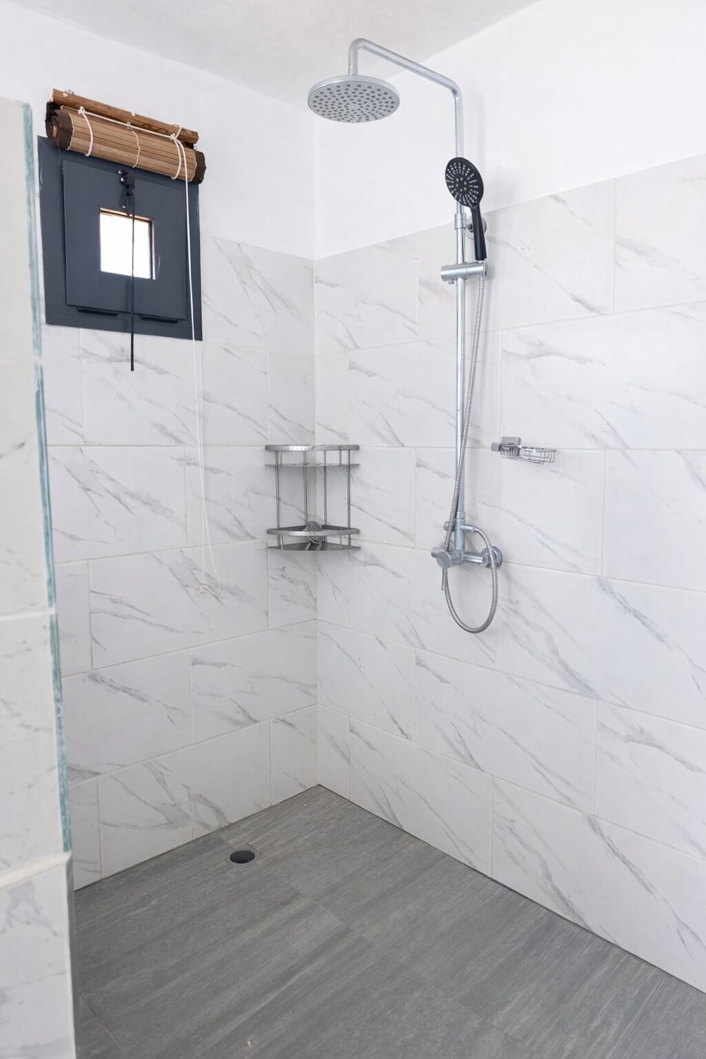 A modern shower area with a handheld showerhead, a wall-mounted faucet, and a glass-enclosed shelf unit.