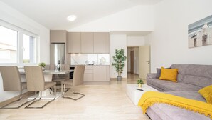 A modern apartment with a dining area, kitchen, and living room. - Stylish Two-Bedroom Apartment with Spacious Sea-View Terrace & Shared Pool (Novalja)