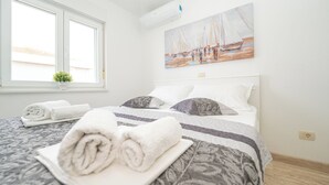 A bedroom with a bed, pillows, a painting, a window, and a potted plant. - Stylish Two-Bedroom Apartment with Spacious Sea-View Terrace & Shared Pool (Novalja)