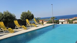 A clear blue pool with yellow lounge chairs and a view of the sea. - Stylish Two-Bedroom Apartment with Spacious Sea-View Terrace & Shared Pool (Novalja)