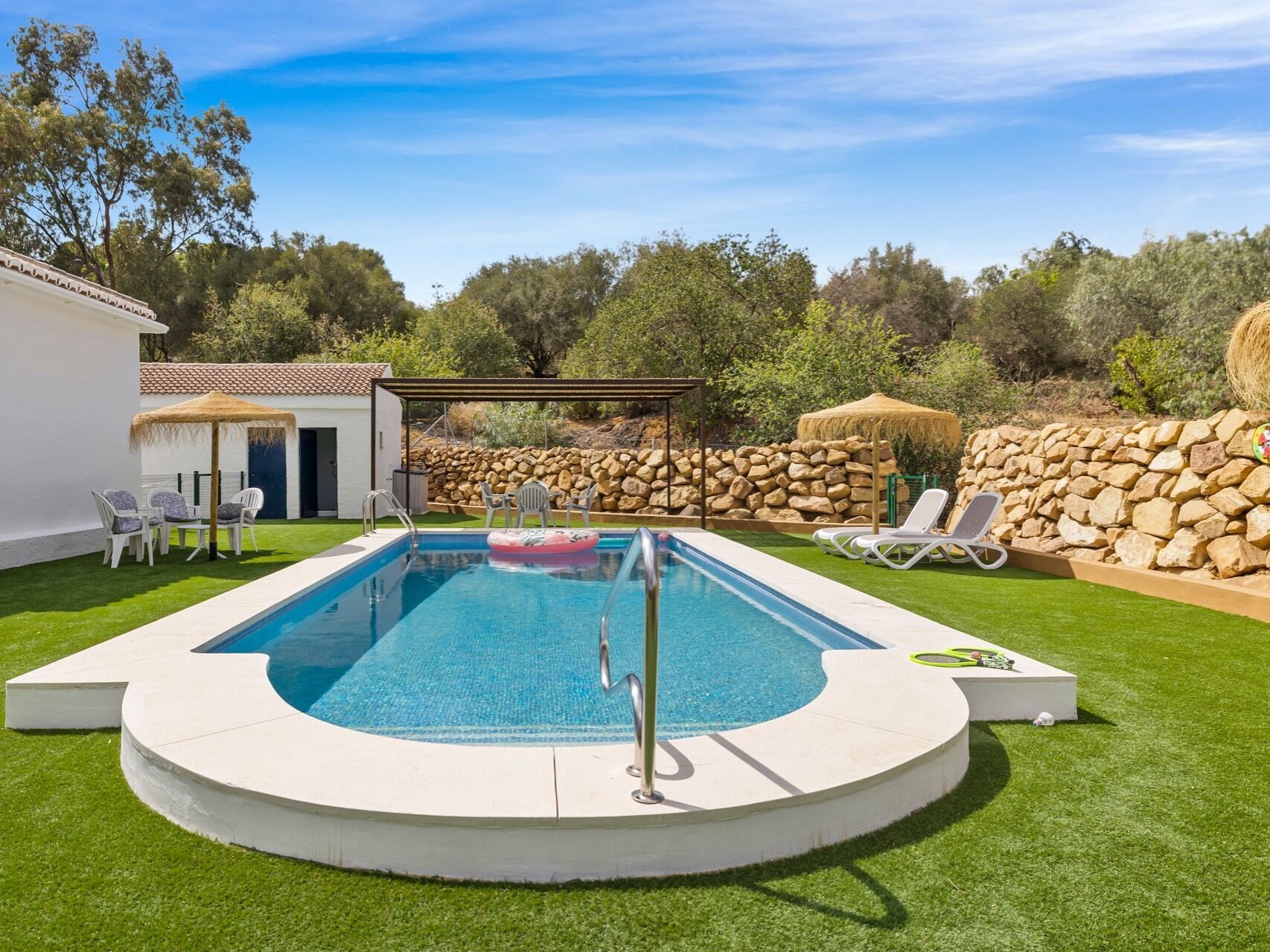 A swimming pool with a stone wall and a grassy area.