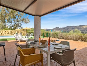 An outdoor dining area with a table set for four, surrounded by wicker chairs, overlooking a pool and a mountainous landscape. - Beautiful 3-bedroom villa with AC and private pool in Pizarra (Pizarra)