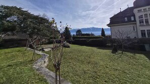 Un jardín bien cuidado con un sendero de piedra, un árbol pequeño y un edificio con techo oscuro y paredes blancas.