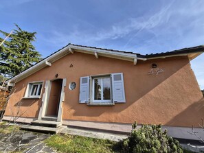 Una casa de dos pisos con fachada marrón, contraventanas blancas y un pequeño porche.