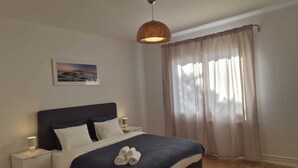 Un dormitorio ordenado con cama, lámparas de noche, un cuadro en la pared y una ventana con cortinas.