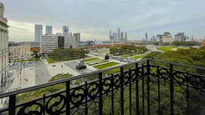 Paisagem urbana com edifícios modernos, uma praça central com uma estátua e uma área de parque.