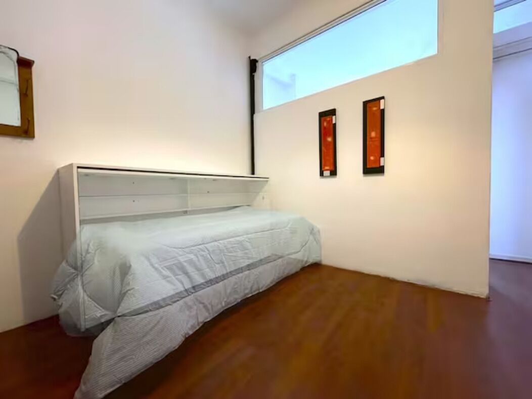 Ein Zimmer mit einem Bett, einer Projektionsleinwand und zwei gerahmten Kunstwerken an der Wand.