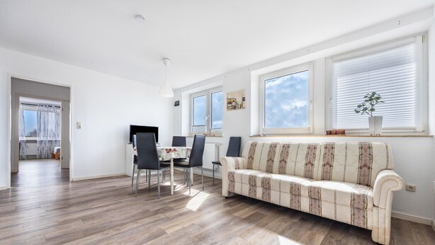 Una sala de estar moderna con un sofá, una mesa de comedor, sillas y ventanas amplias.