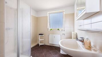 Ein Badezimmer mit Dusche, Waschbecken und Fenster.