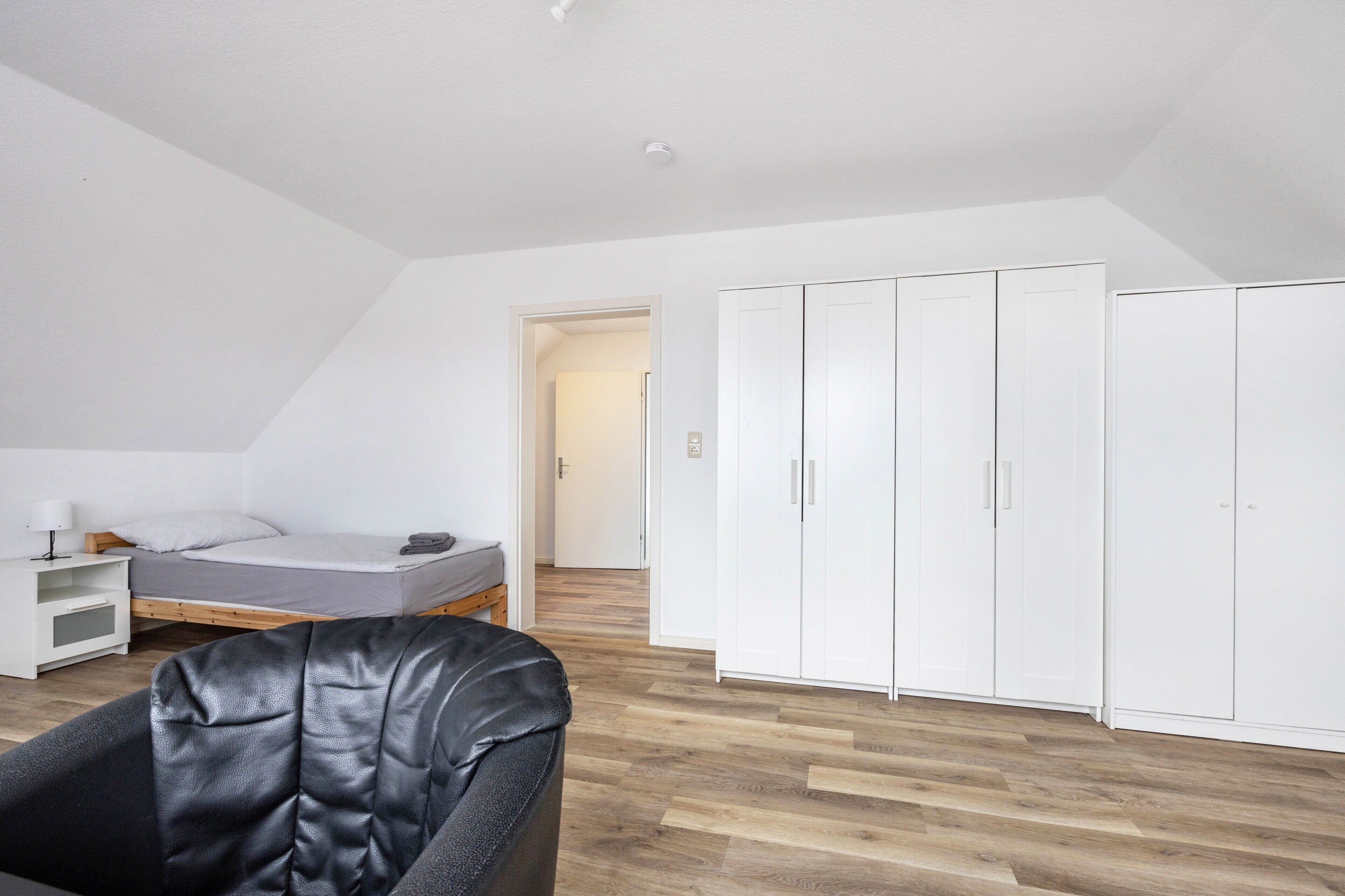 A bedroom with a bed, a chair, a wardrobe, and a nightstand.