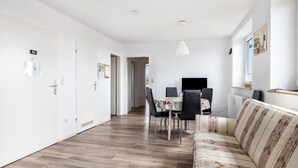 Un interior moderno con piso de madera, un comedor con mesa y sillas, un sofá y una lámpara colgante.