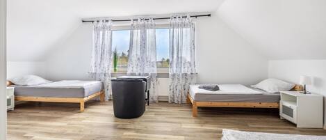 Une chambre avec deux lits, une poubelle noire et une fenêtre avec des rideaux.