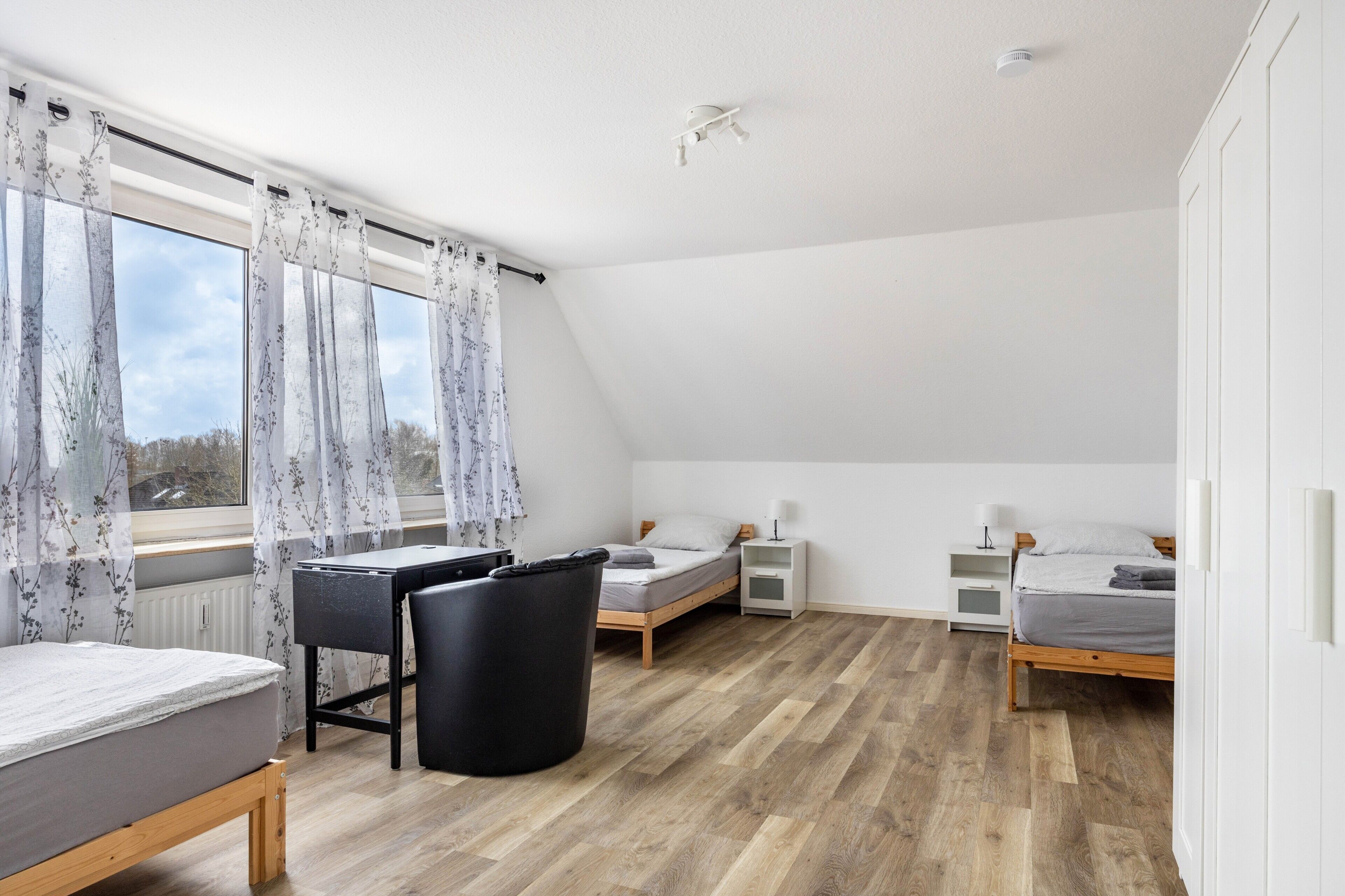 Ein Schlafzimmer mit Schreibtisch, zwei Betten, Heizkörper und einem Fenster mit Vorhängen.