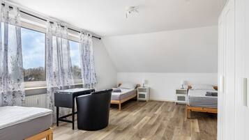 Ein Schlafzimmer mit Schreibtisch, zwei Betten, Heizkörper und einem Fenster mit Vorhängen.